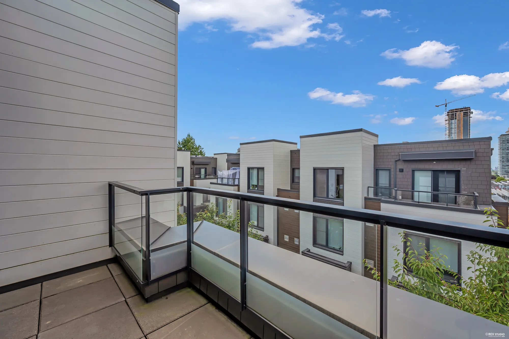 The balcony off the primary bedroom: pavers, glass railings, the rooftops of the complex and towers in the distance under a blue sky