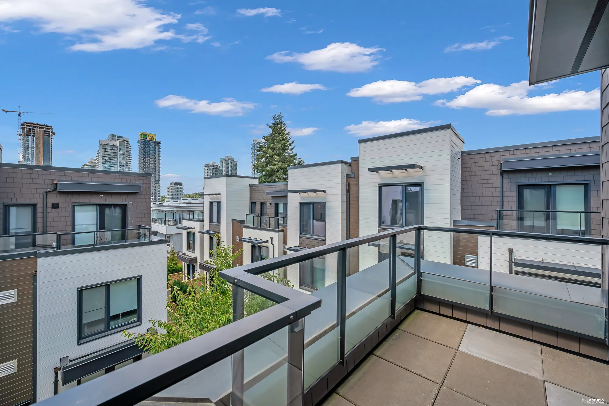Over the balcony railing to the neighbouring rooftops, a tall fir and towers in the distance