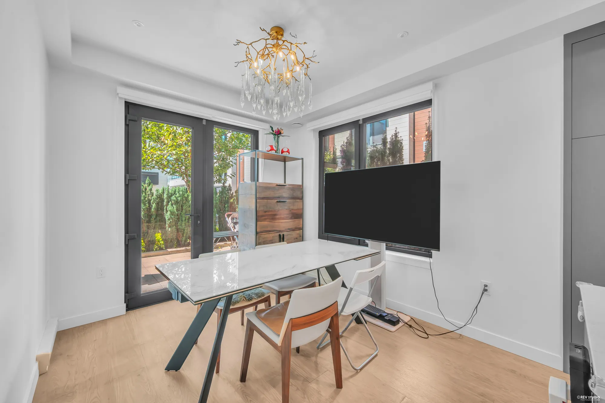 The dining room: a pair of glass doors to the back patio, a window, a crystal chandelier, a stone-look table and chairs, a TV on a stand