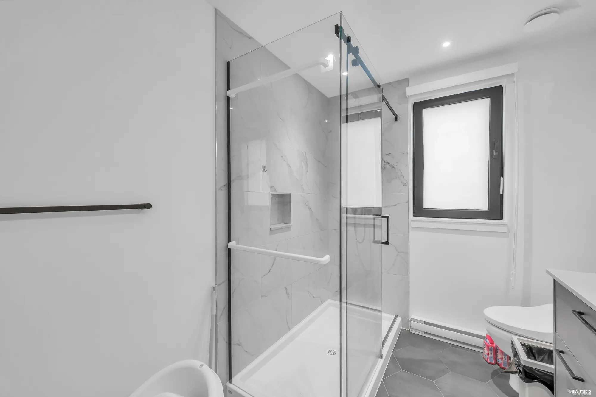 The shower in the primary bathroom: a sliding glass door, marble-look tile and a niche, a frosted window