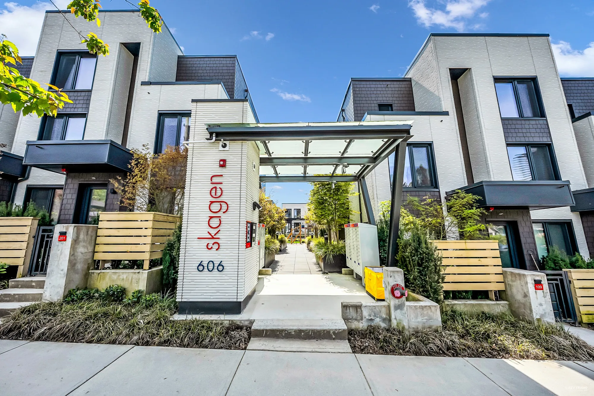 The entrance to Skagen from the street: a white pillar with the name skagen and the number 606 in red, a glass canopy over the path into the complex, townhomes on either side
