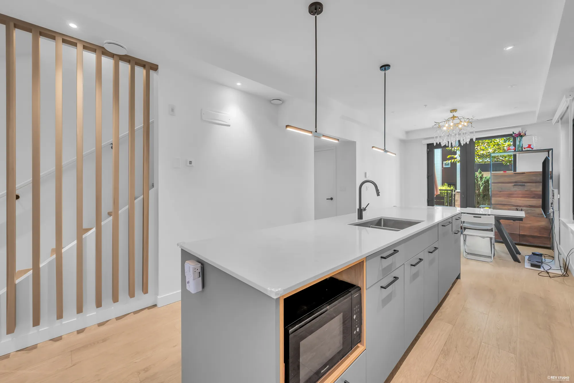 The island toward the dining room: the sink and tap, a microwave set into the end of the island, pendant lights, the dining room&rsquo;s glass doors beyond