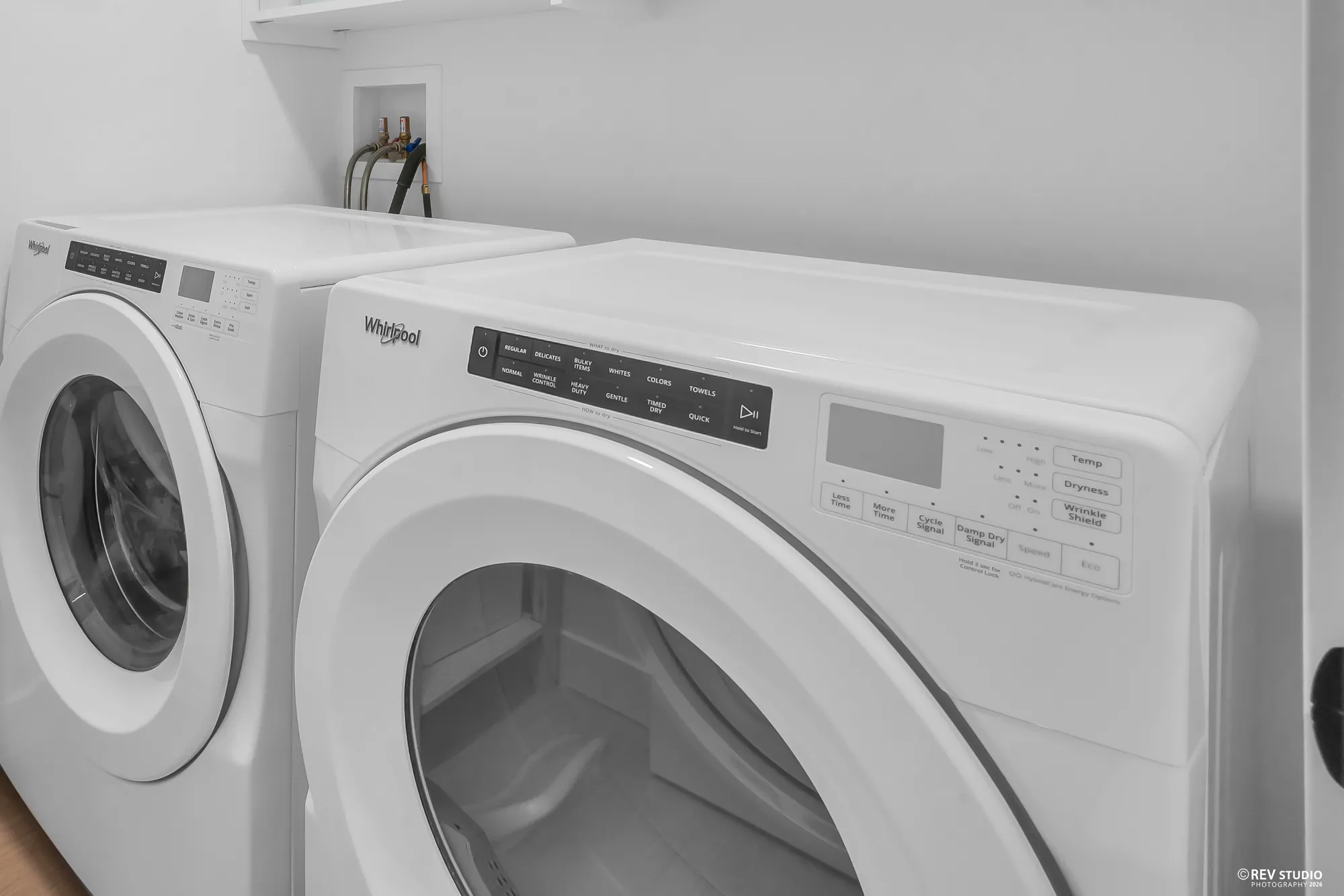 The laundry room: a white front-load washer and dryer side by side, the water connections in the wall above