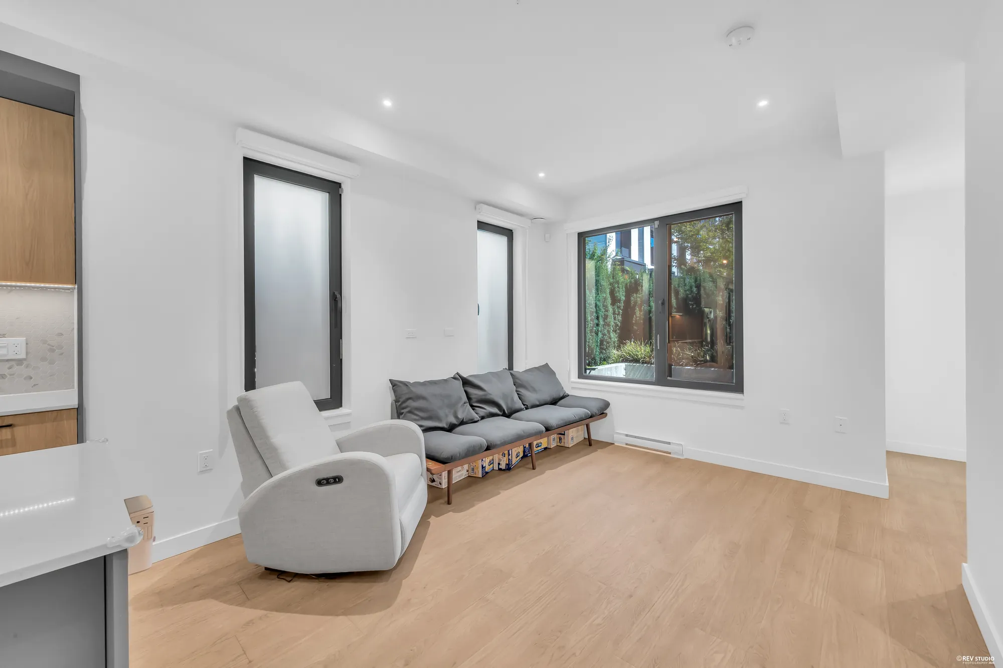 The living room: a long cushioned bench under two tall frosted windows, a grey recliner, a wide window onto the front patio, wood-look floors