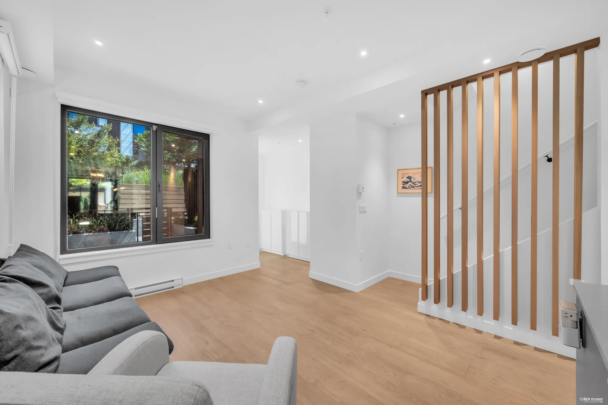 The living room beside the stair: a screen of vertical wood slats along the stair, the front window, a sofa in the foreground