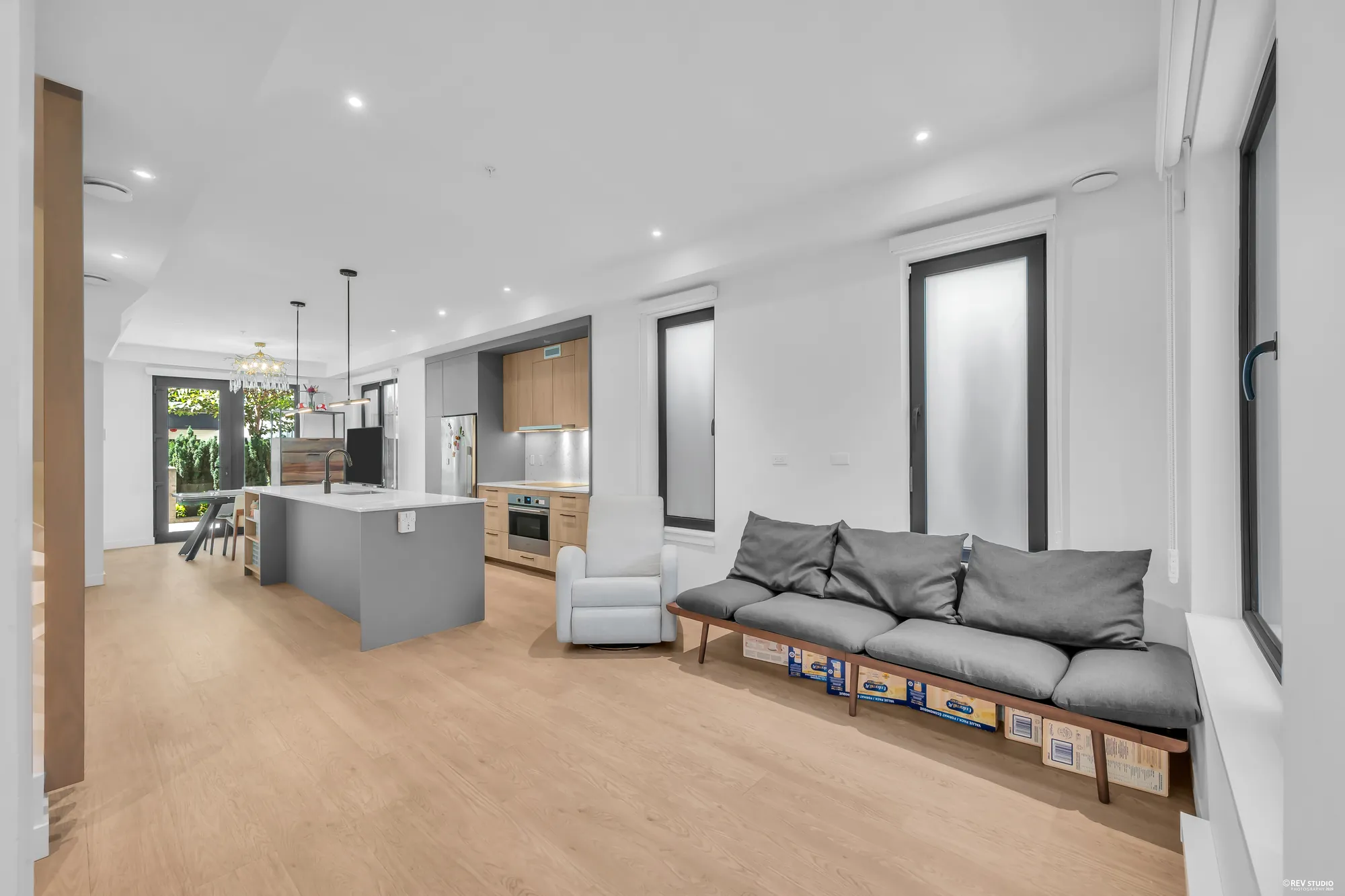 From the living room through the kitchen to the dining room: the grey island, the wall of cabinets, the dining room&rsquo;s glass doors at the far end