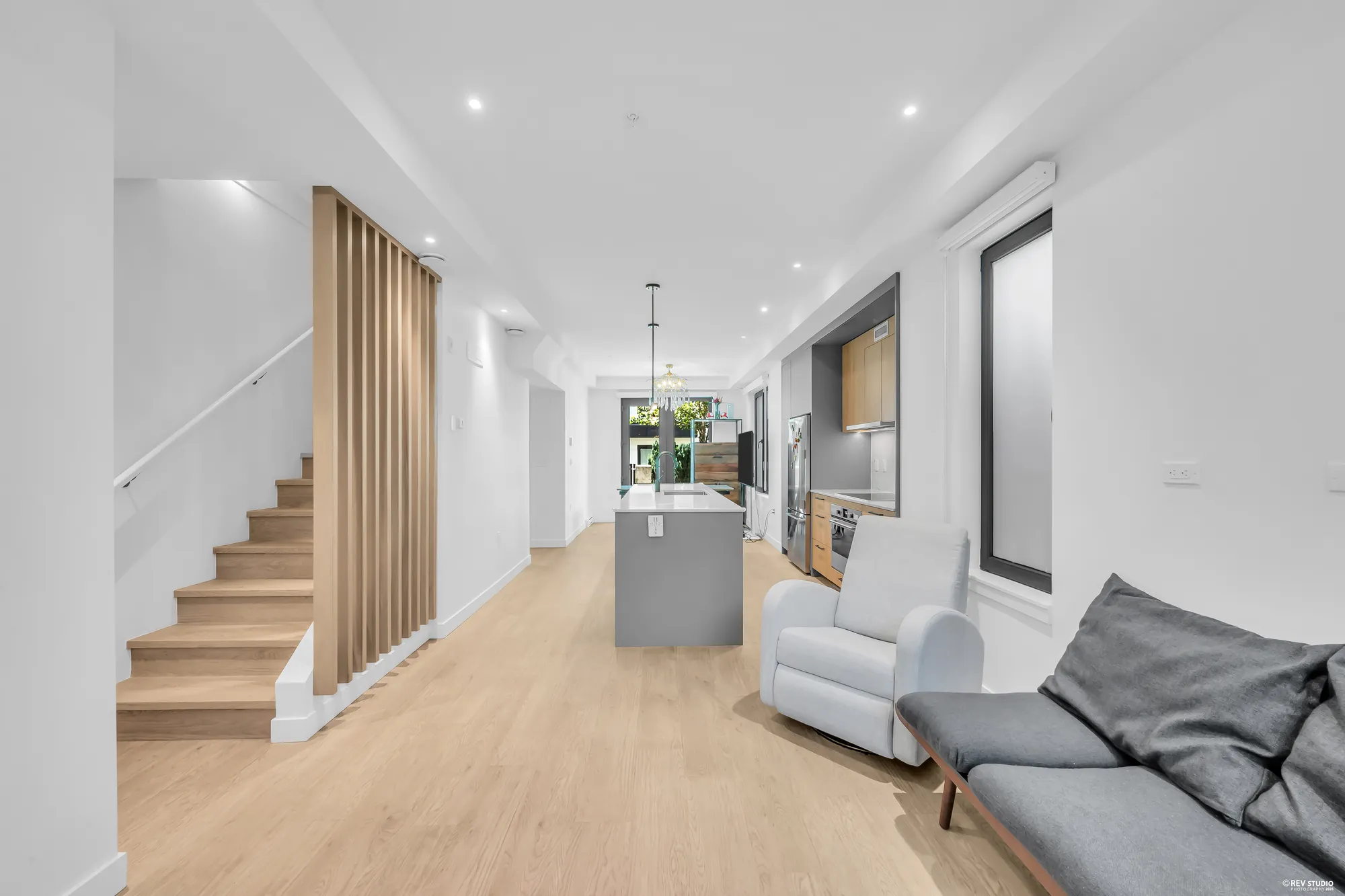 The stair and its slat screen at the left, the kitchen island beyond, a recliner and the bench at the right
