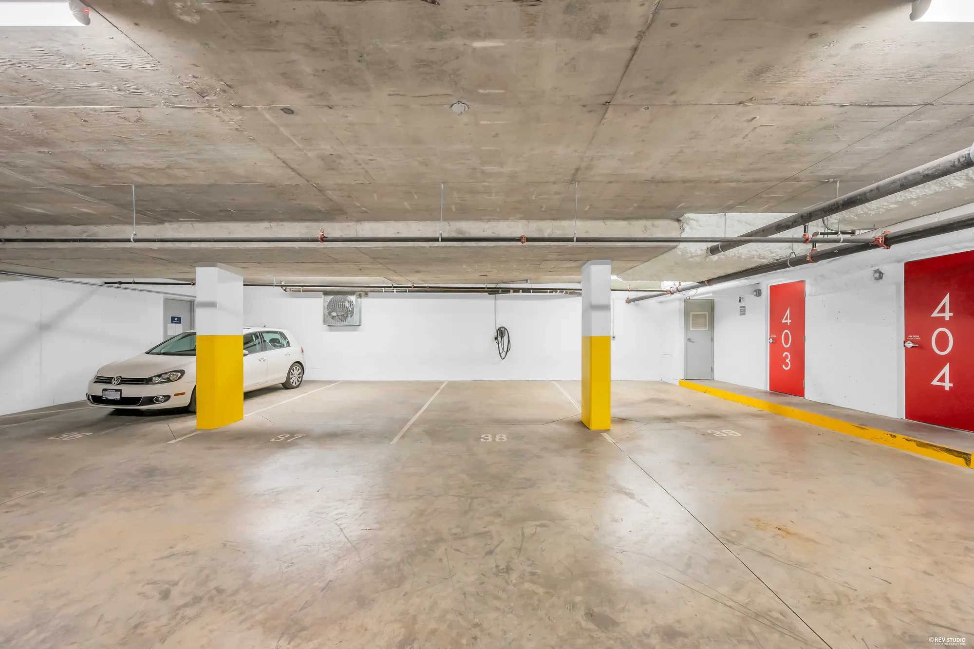 The underground parking: numbered stalls between yellow-banded columns, an EV charger on the far wall, a red door marked 404 at the right