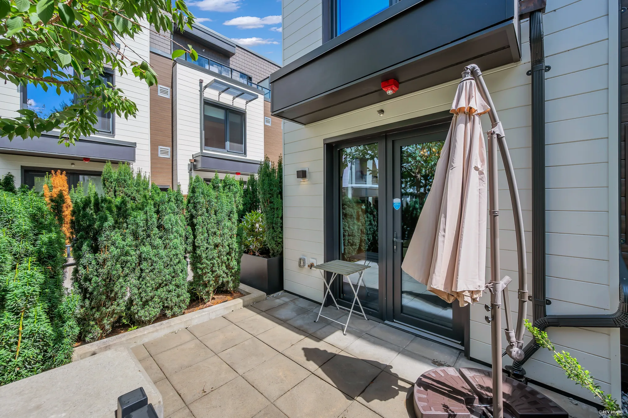 The back patio toward the house: the dining room&rsquo;s pair of glass doors, a wall light, a small folding table and the umbrella