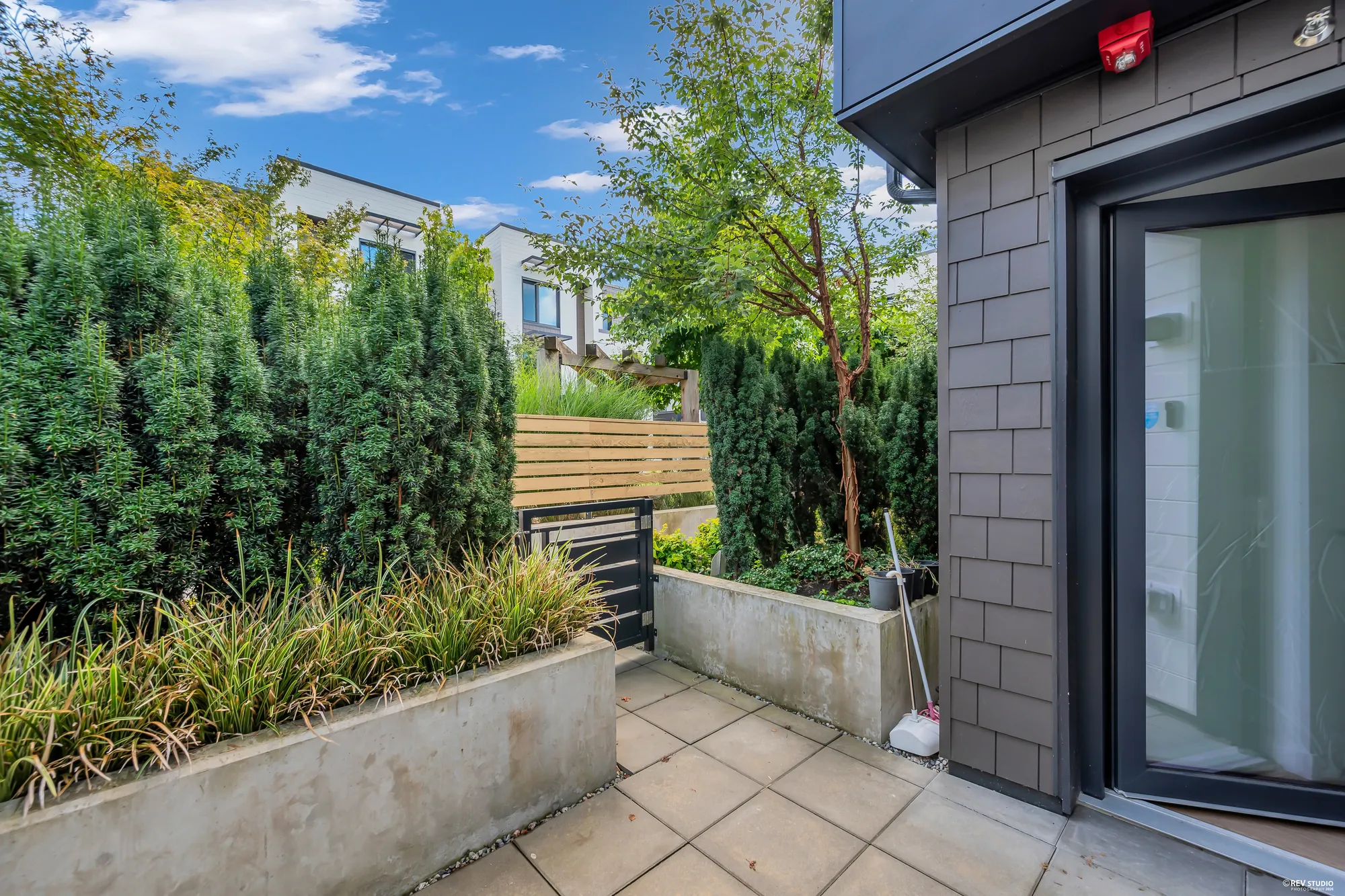 The front patio toward the gate: the planter at the left, the hedges, the glass front door in the shingled wall at the right