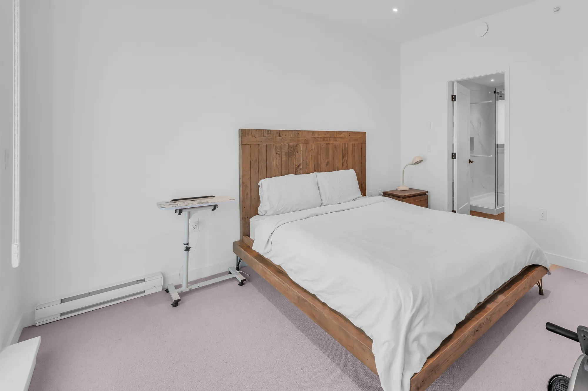 The primary bedroom: a bed with a wood headboard, a nightstand and lamp, the door to the bathroom at the right, carpet